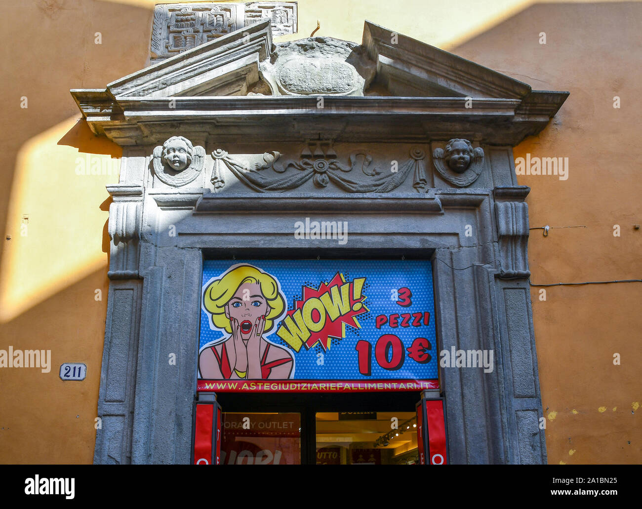 Close-up of an ancient stone door frame and tympanum with a shop sign in pop art style in the historical centre of Lucca, Tuscany, Italy Stock Photo