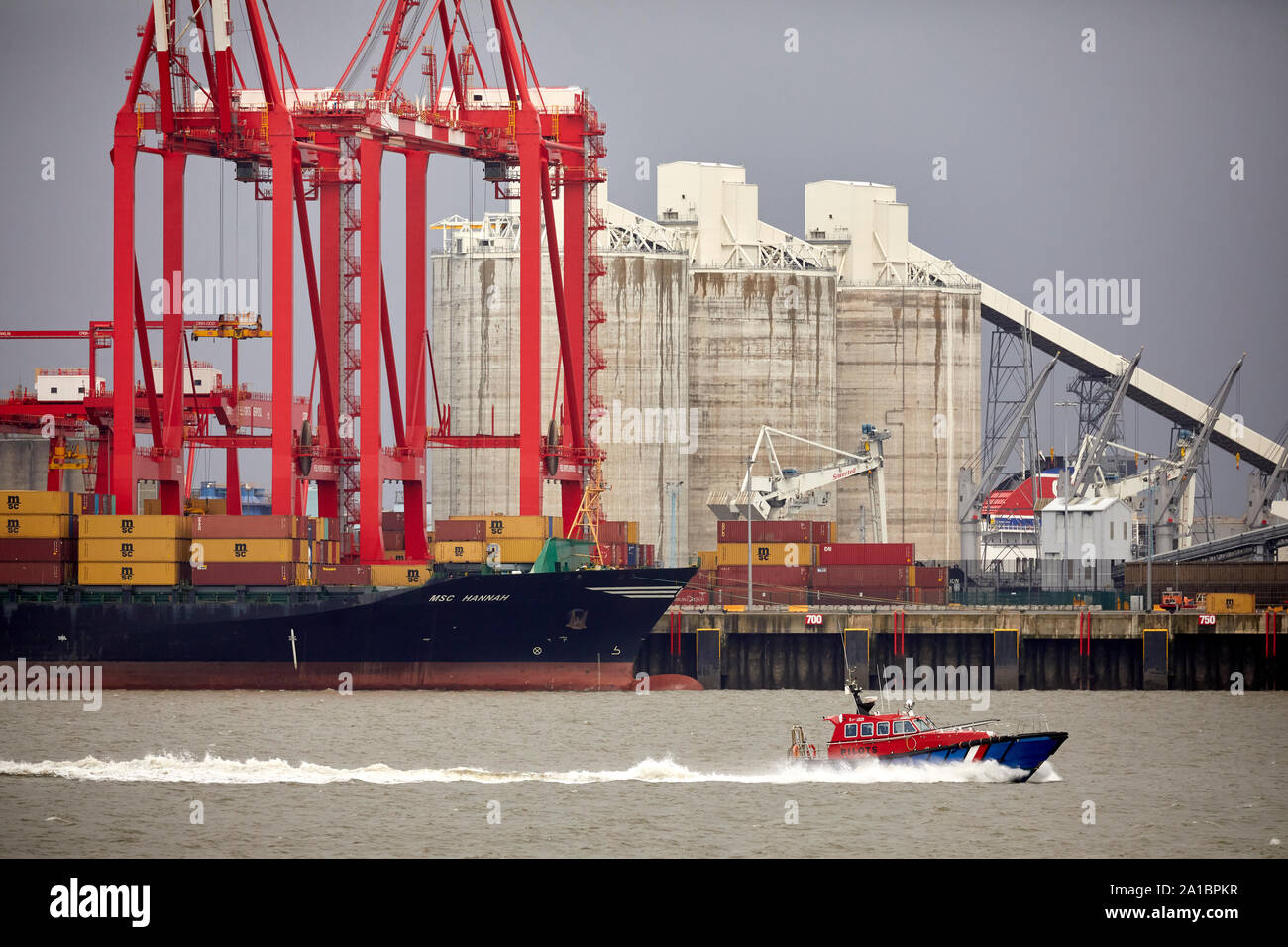 Large cargo container ship unloading at  Hornby Dock, Port of Liverpool, Bootle passed by a smaller Pilot boat in the River Mersey Stock Photo