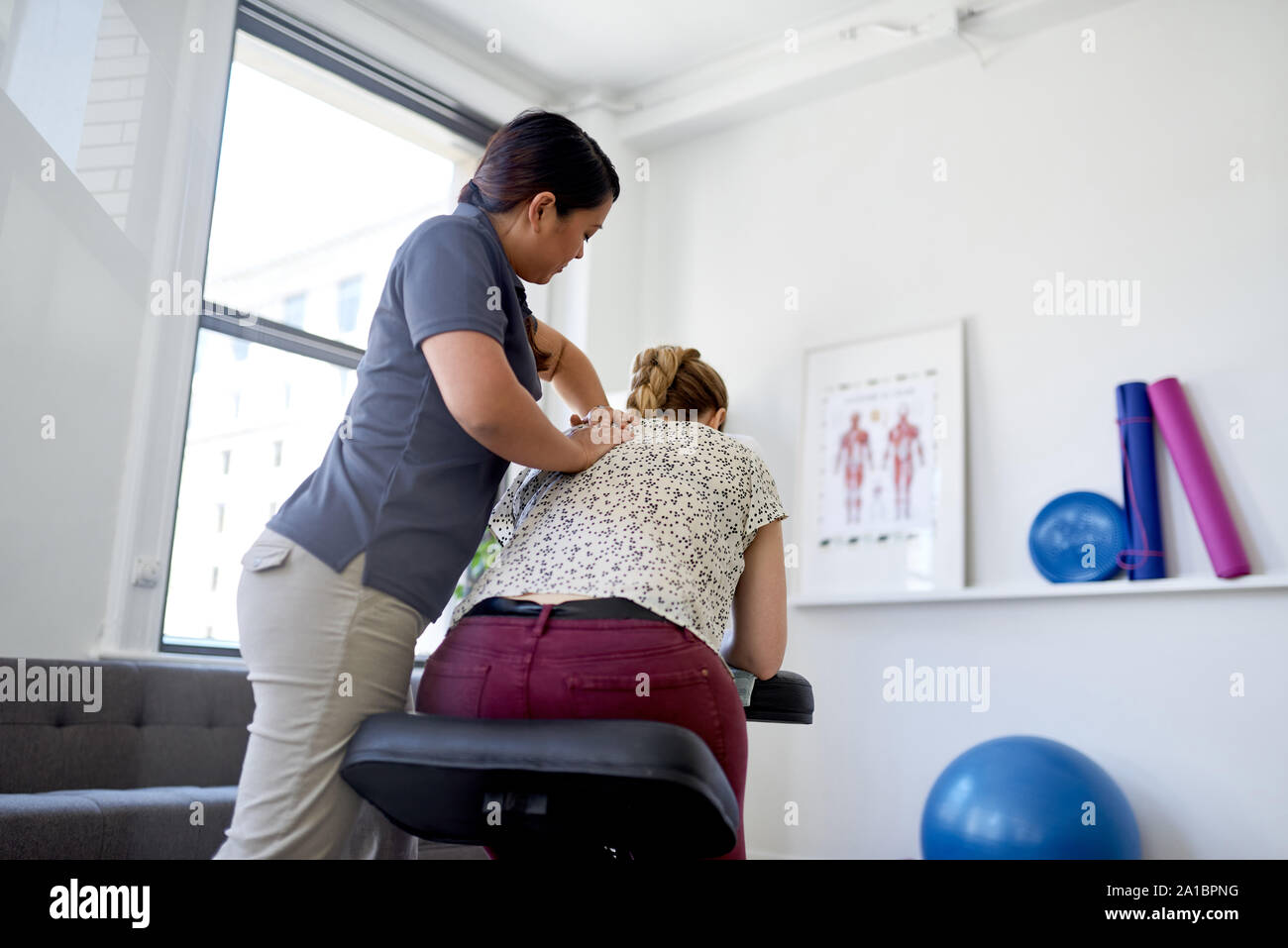 Chinese woman massage therapist giving a neck and back pressure treatment to an attractive blond client at her workplace in a bright office Stock Photo