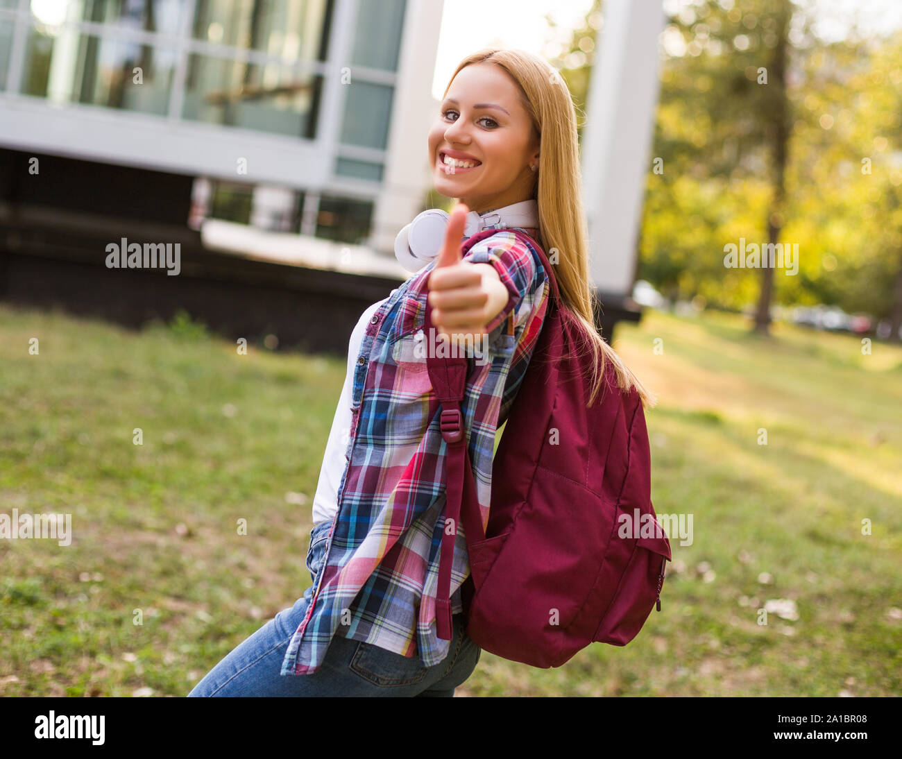 Portrait of beautiful female student showing thumb up while standing ...