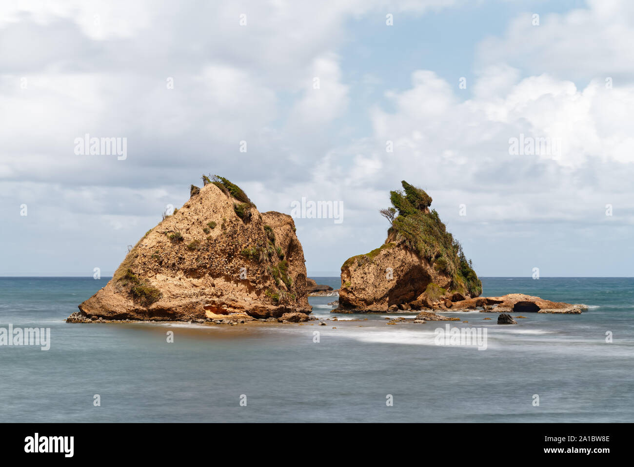 View to two rugged rocky islands in calm coastal waters against cloudy sky with cloud gap, water movement in long exposure - Location: Caribbean, isla Stock Photo