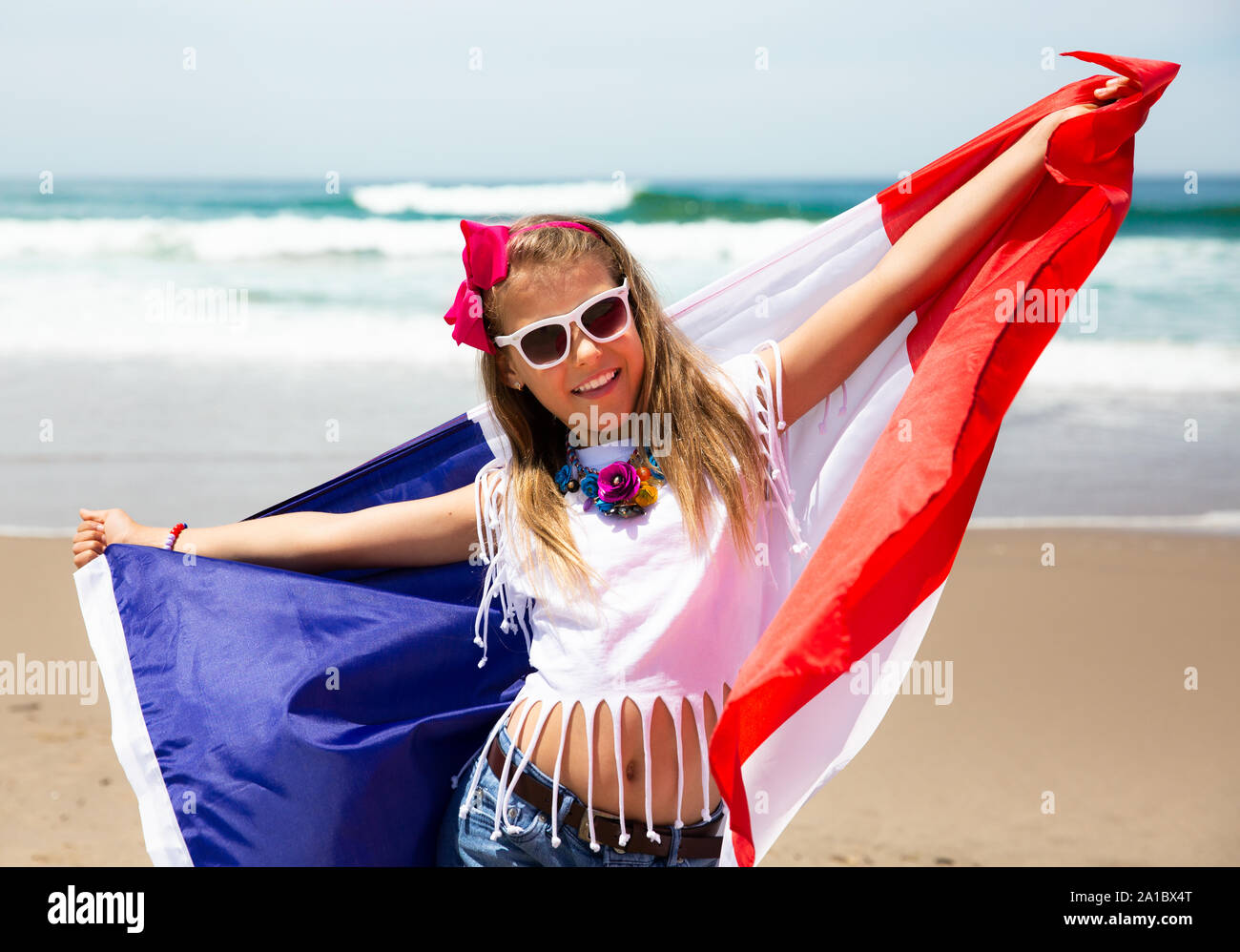 Happy French girl carries fluttering blue white red French flag of France against blue sky and Atlantic ocean background Stock Photo