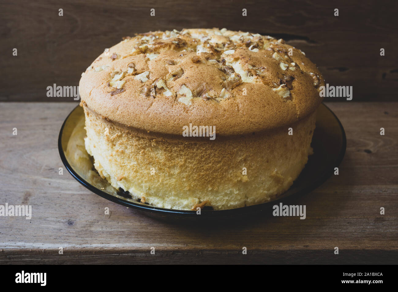 Cotton sponge cake with walnuts on top and raisins (dried black grapes) at the bottom, ready to eat, on rustic wooden table, homemade. Vintage toned Stock Photo