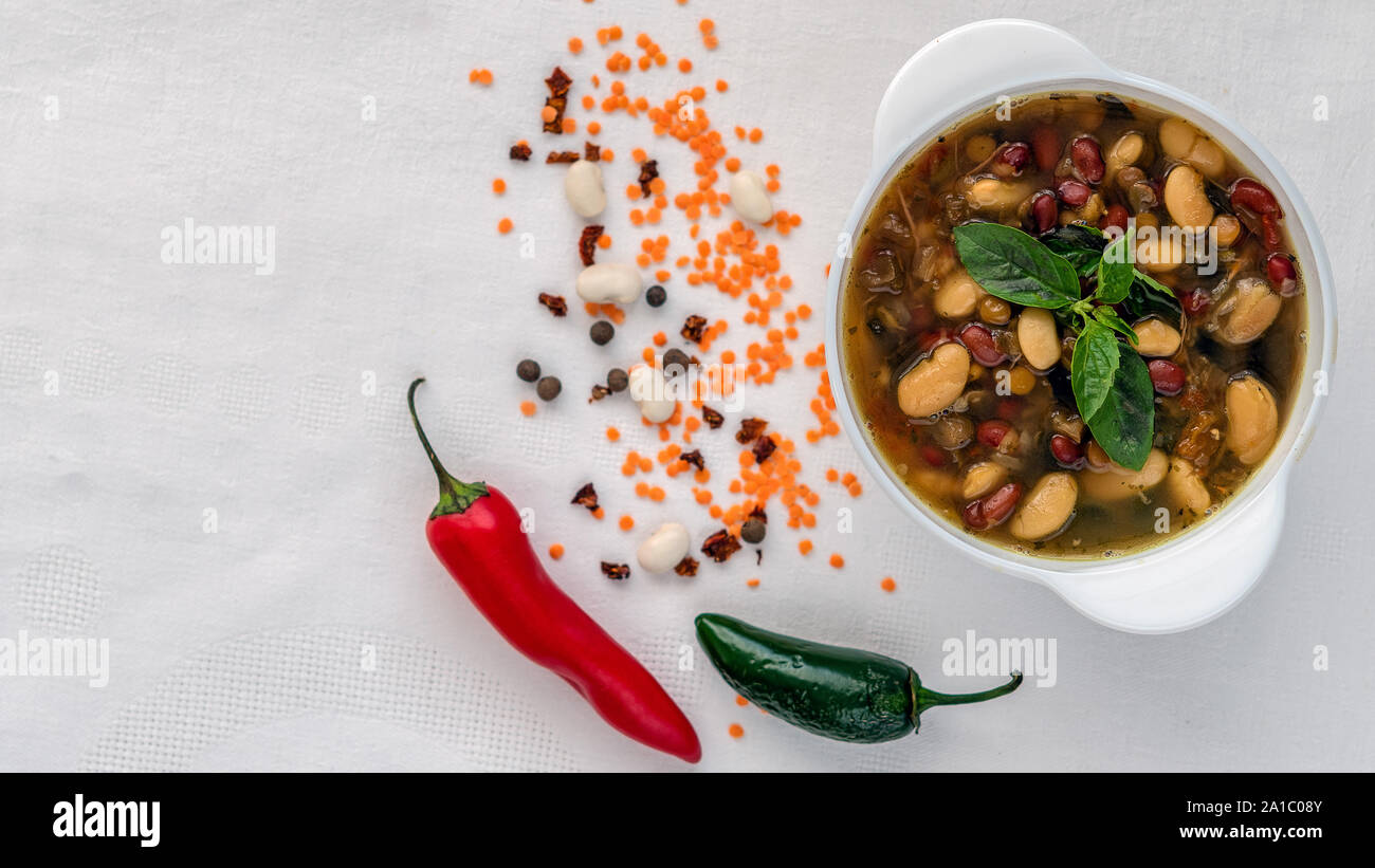 Mexican soup of seven kinds of beans, close-up, on a white linen background surrounded by red and green peppers and beans Stock Photo
