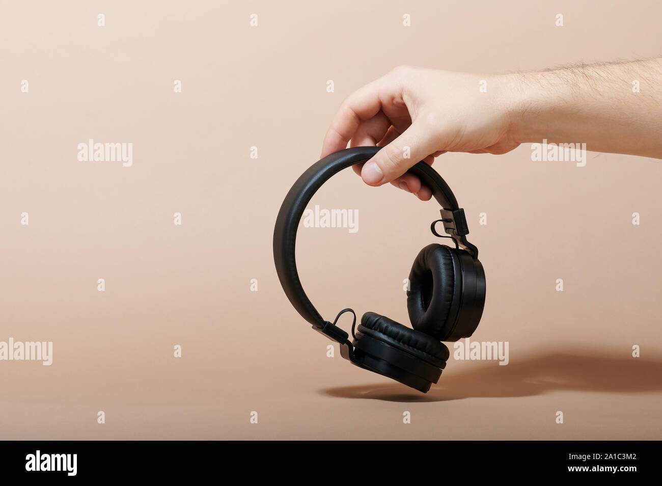 Hand hold wireless headphones isolated on beige background Stock Photo