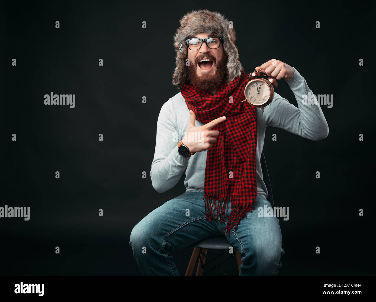 Portrait of amazed man with beard pointing at alarm clock Stock Photo