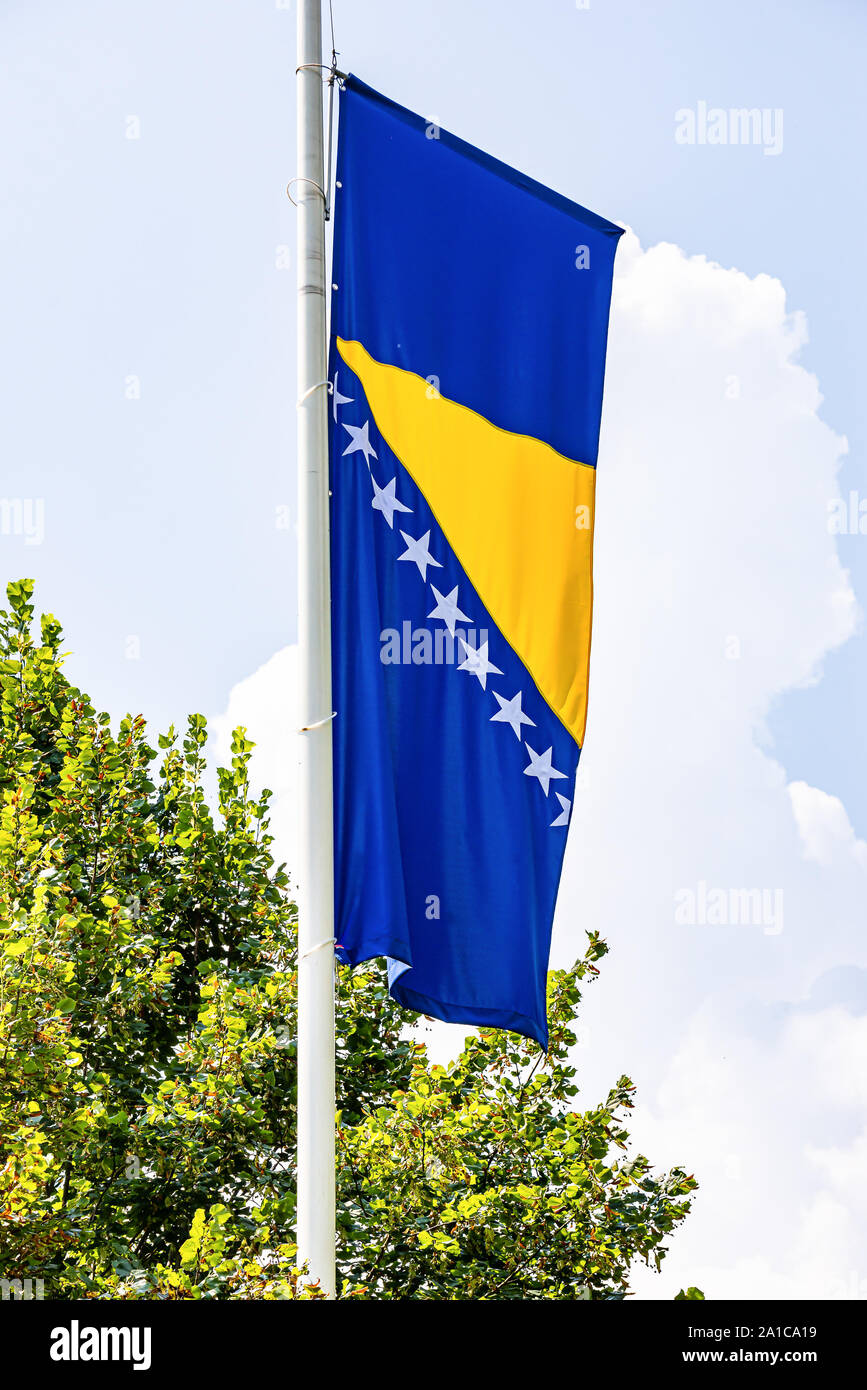Banner flag of Bosnia and Herzegovina in the wind with sky and tree in background Stock Photo