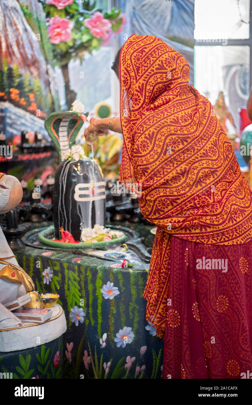 An unidentified devout Hindu woman pours milk on a Shiva lingam at a temple in Jamaica, Queens, New York City. Stock Photo