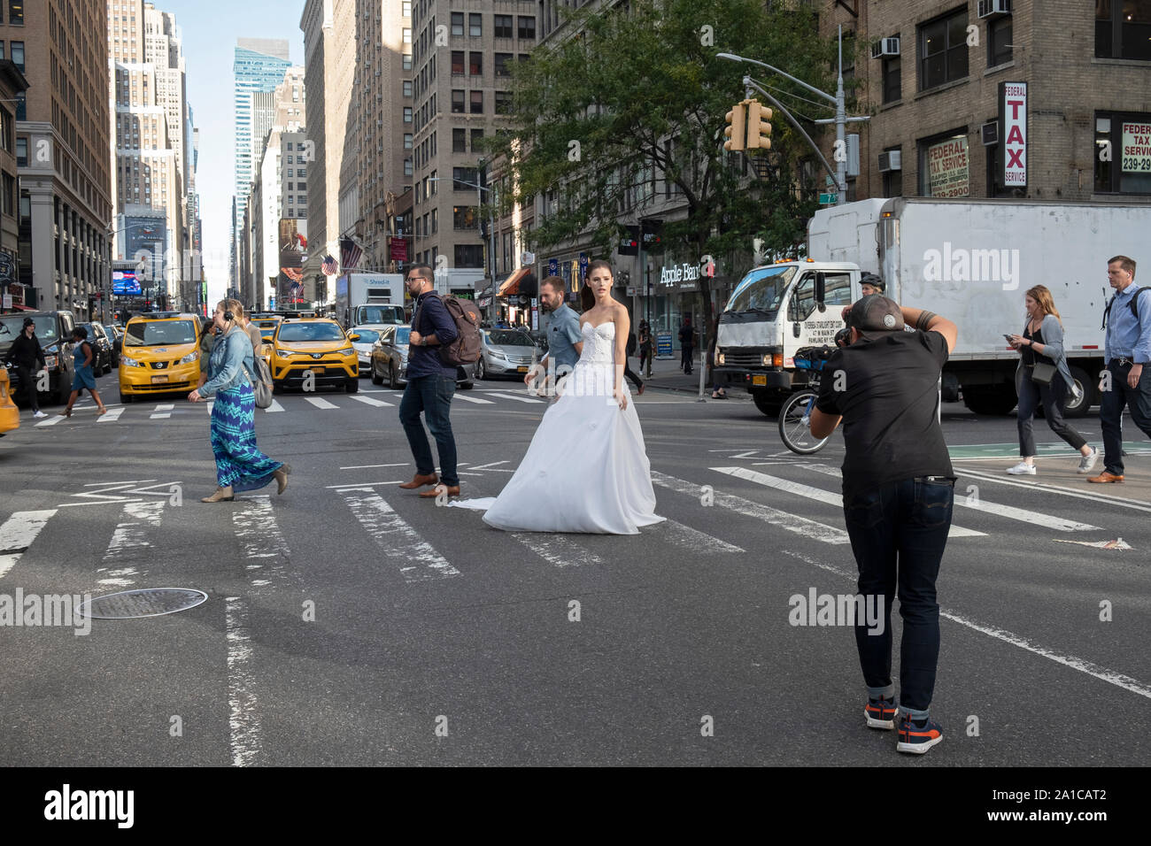 A model in a bridal gown poses for photos on a busy street corner - 7th ave. & West 29th Street -  in Manhattan, New York City. Stock Photo