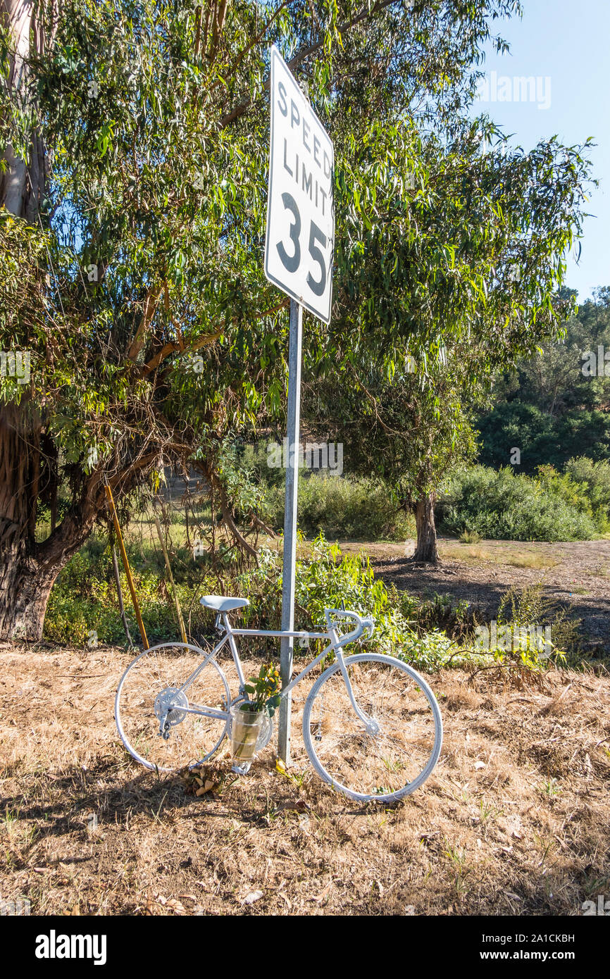 Roadside memorial to a bikers death with a bicycle painted all white, flowers and a vase on the side of Modoc Road in Santa Barbara, California. Stock Photo