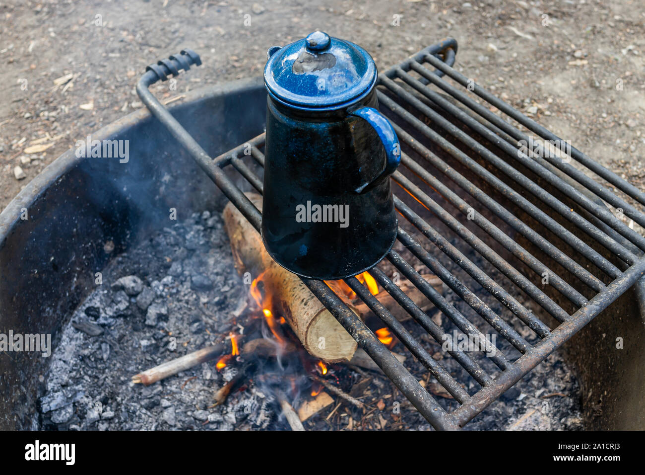 Blue tea water kettle on grill in fire pit at campground with red flame