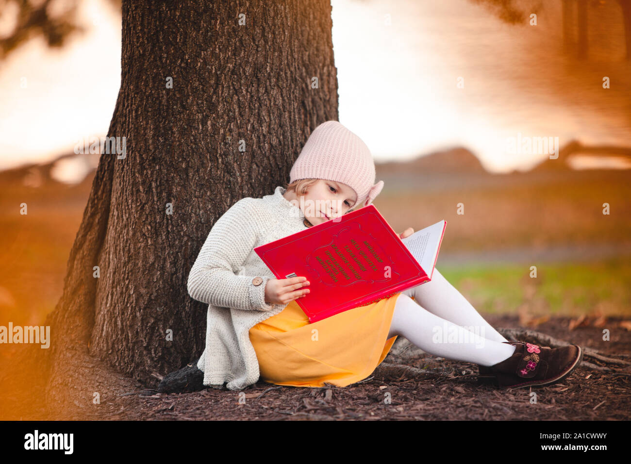 Little caucasian girl is reading the book under the fall tree Stock Photo