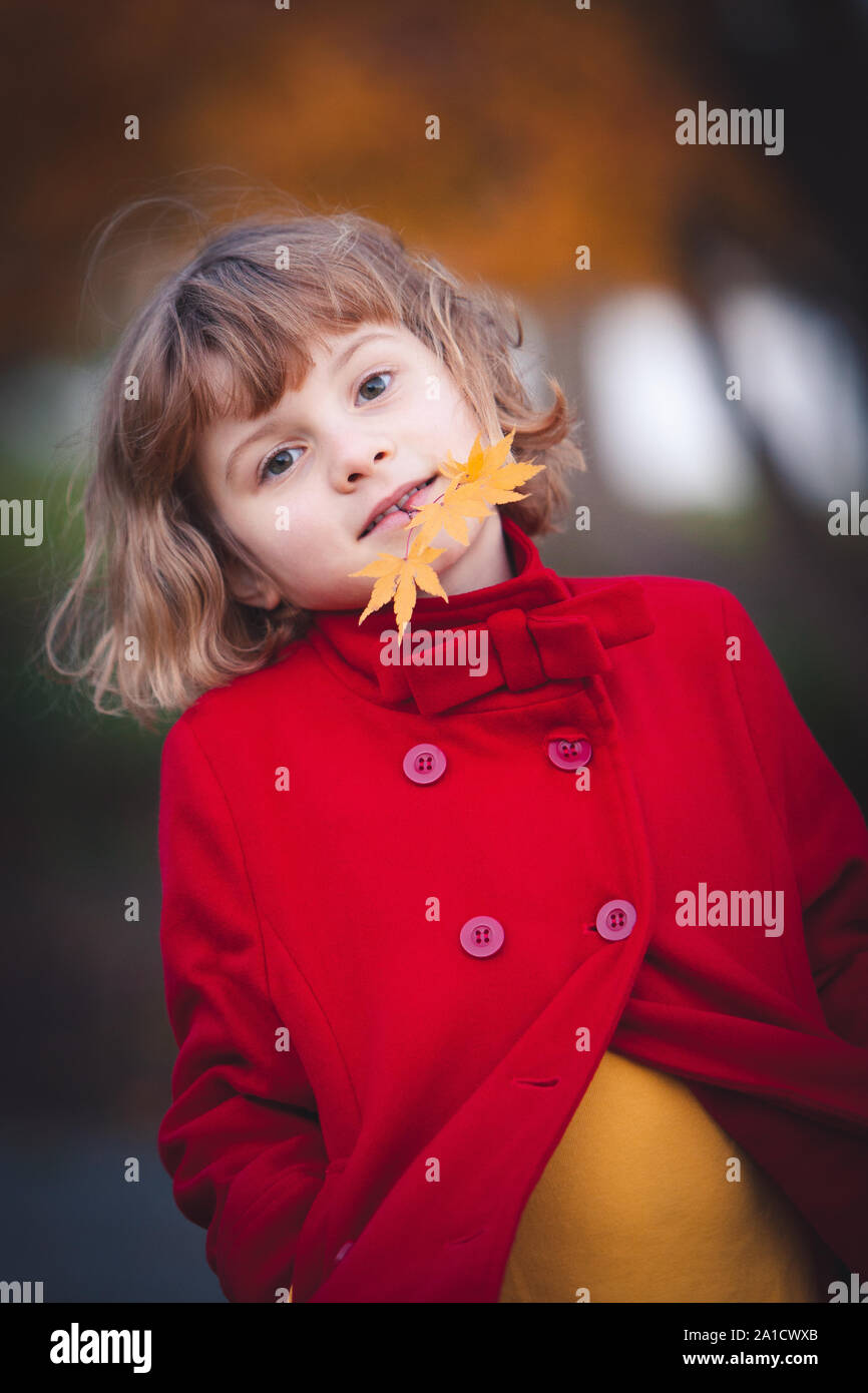 Little caucasian girl wearing red coat is holding fall leaf in her ...