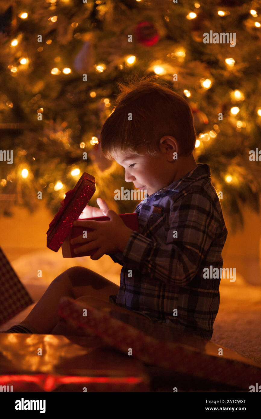 Little caucasian boy is openning his Christmas gift in front of the Christmas tree Stock Photo
