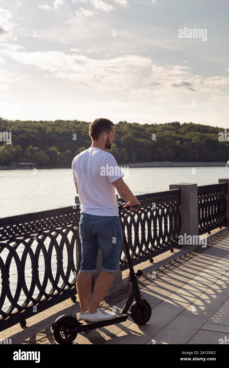 Man riding an ecofriendly electric kick scooter in a park in sunny