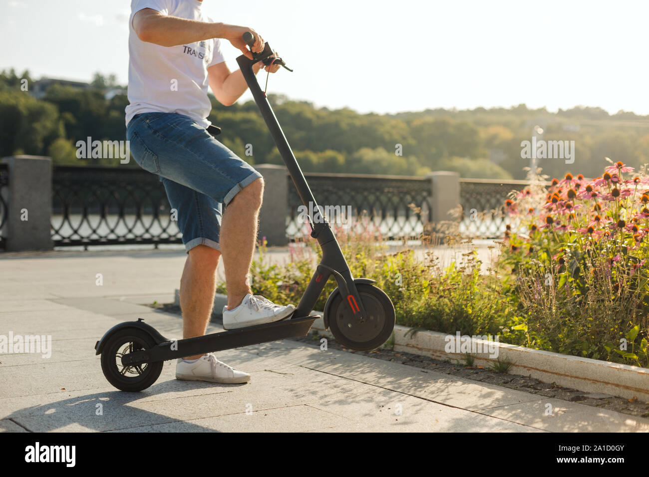 Man riding an ecofriendly electric kick scooter in a park in sunny