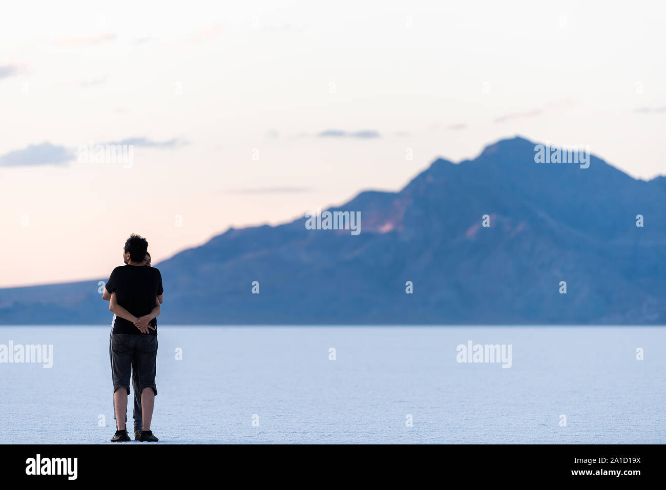 Wendover, USA - July 27, 2019: People couple hugging on white Bonneville Salt Flats near Salt Lake City, Utah and silhouette mountain view Stock Photo