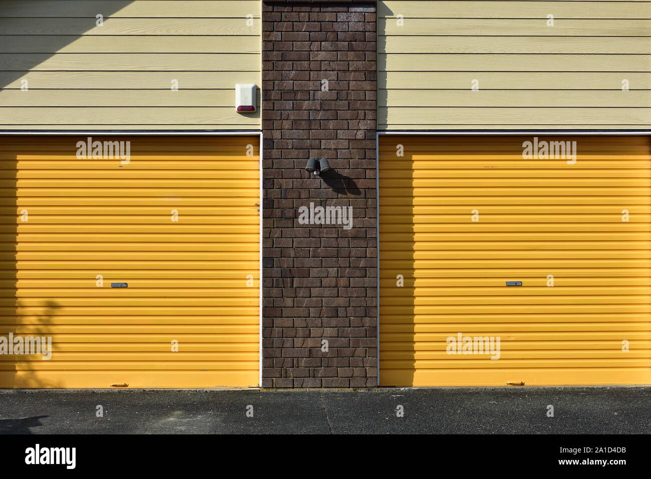 Yellow metal garage gates with brick wall between them and weatherboard cladding above. Stock Photo