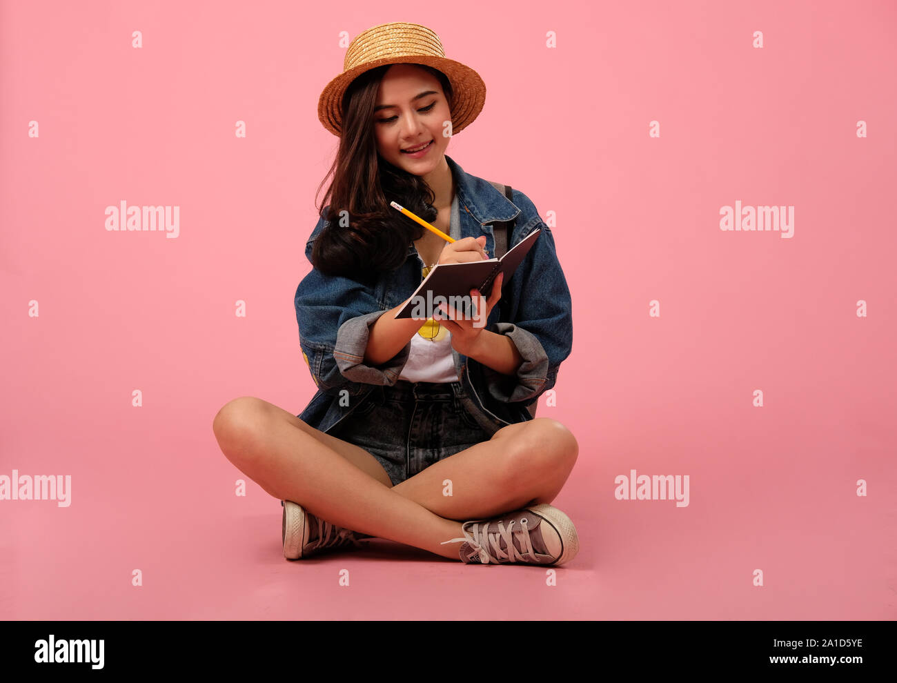 portrait of smiling young asian woman wearing jeans jacket writing note ...