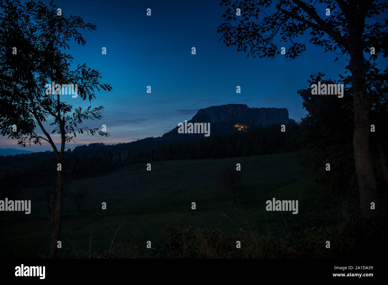 The stone of Bismantova, an isolated impressive spur in the italian appenines region. Blue hour, twilight view, framed by trees. Stock Photo