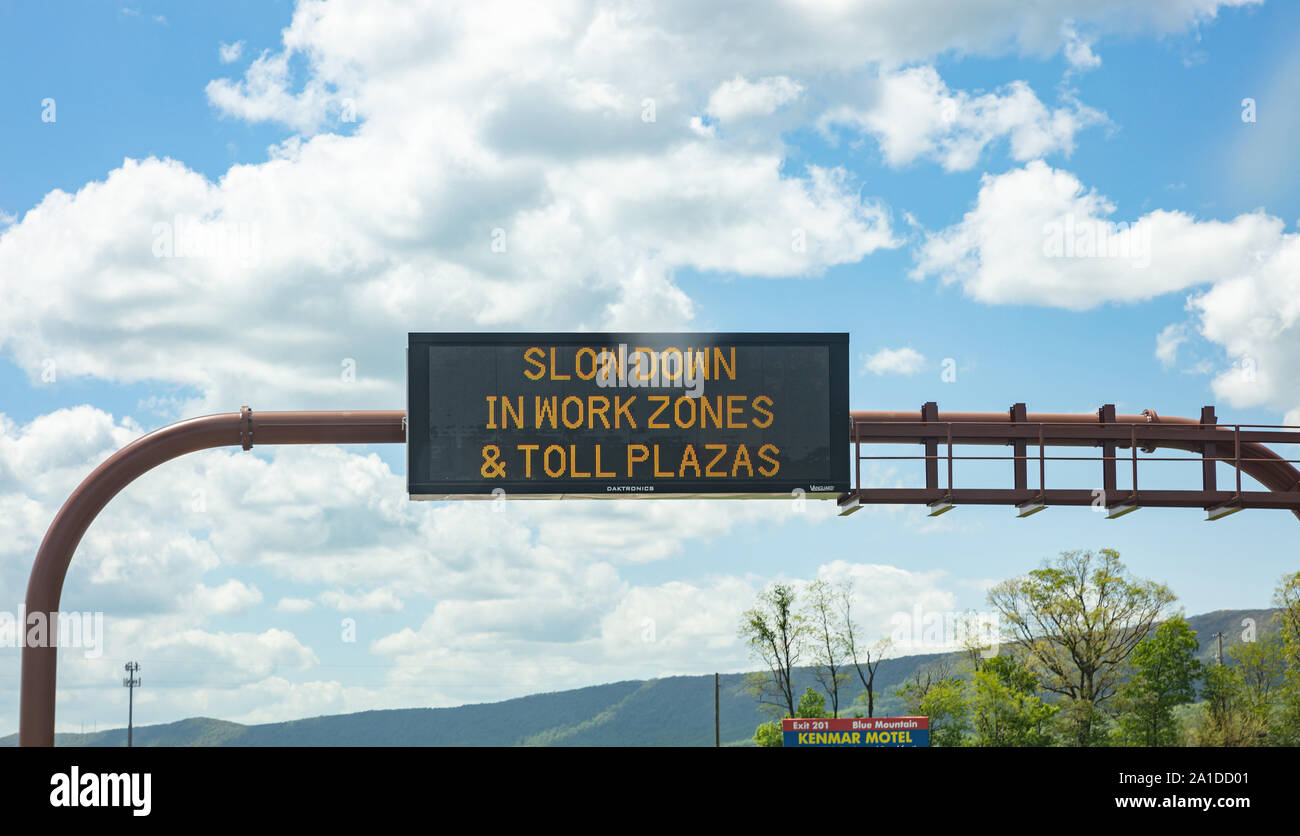 Pennsylvania highway, USA. May 6, 2019: Slow down in work zones and toll plazas Warning led road sign billboard on a highway, cloudy blue sky Stock Photo