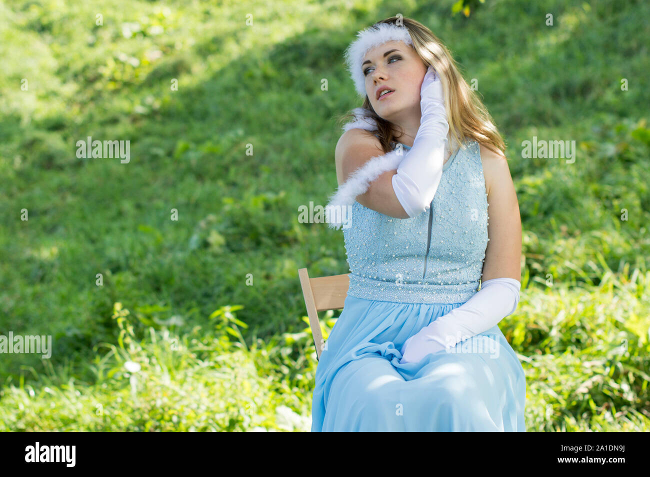 Young girl in white hat, white gloves and a blue dress. The girl holds in her hand a leaf of a green plant. Stock Photo