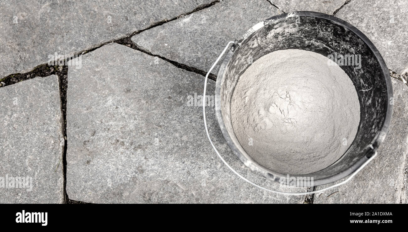 bucket with cement on a grey flagstone floor with unfilled joints Stock Photo