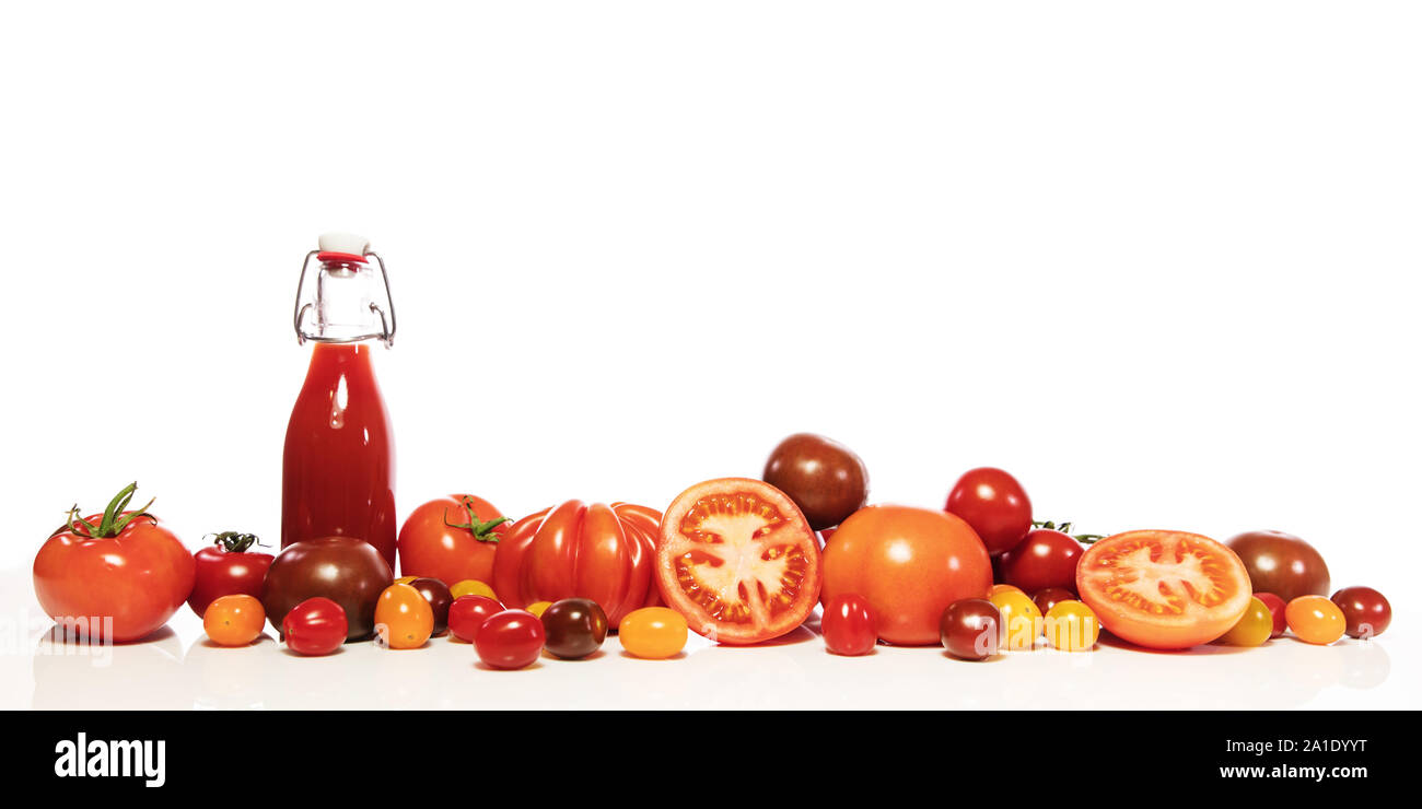 a lot of various tomatoes and a full bottle with juice or tomato sauce, in front of white Stock Photo