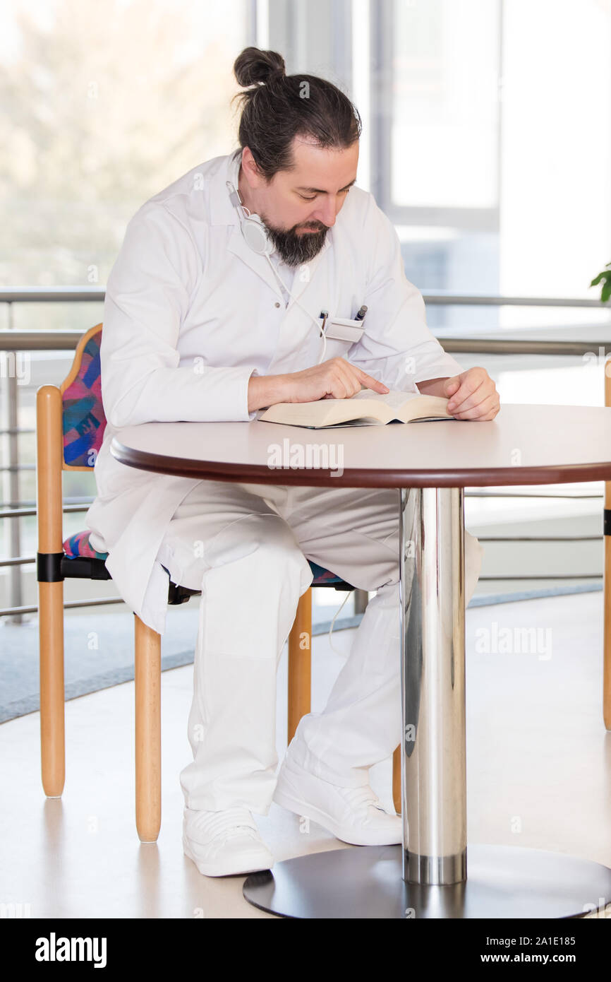 doctor is having a break, sitting on the table and reading a book Stock Photo