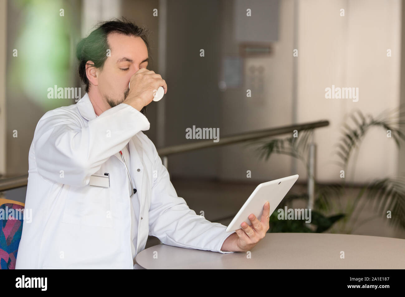 doctor is having a break, sitting on the table and reading his tablet Stock Photo