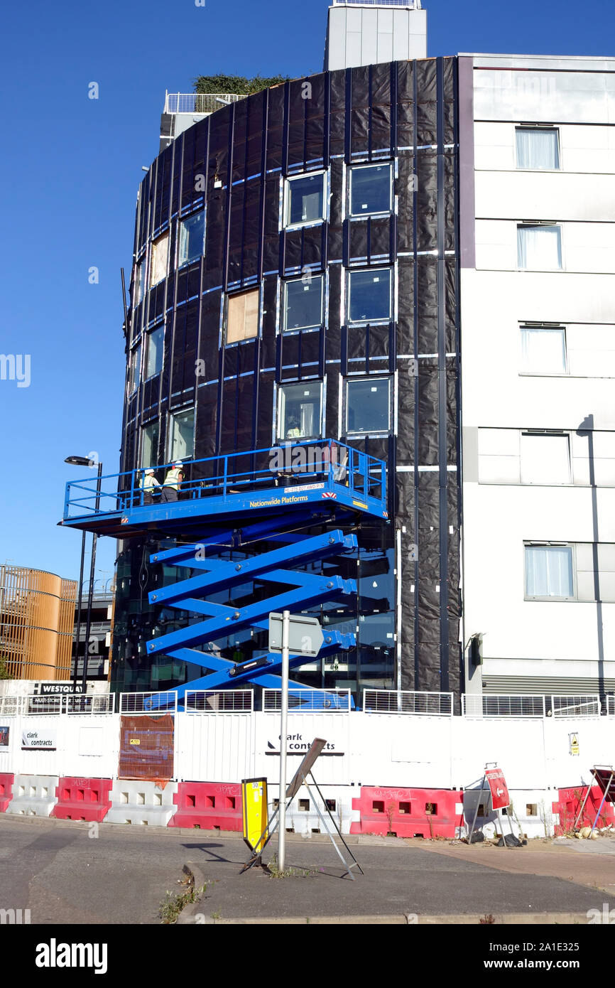 Workmen on heavy duty scissor lift installing cladding on a new build next to Westquay Shopping Centre,Southampton, England Stock Photo