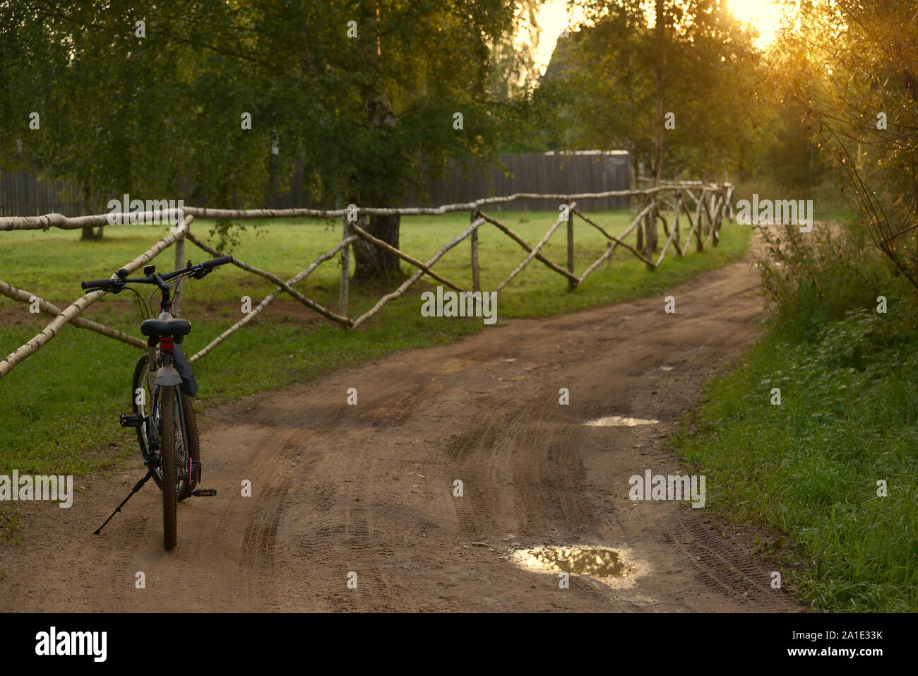 A black bicycle is leaning against a stand on the side of a rural road on an early summer morning. Stock Photo