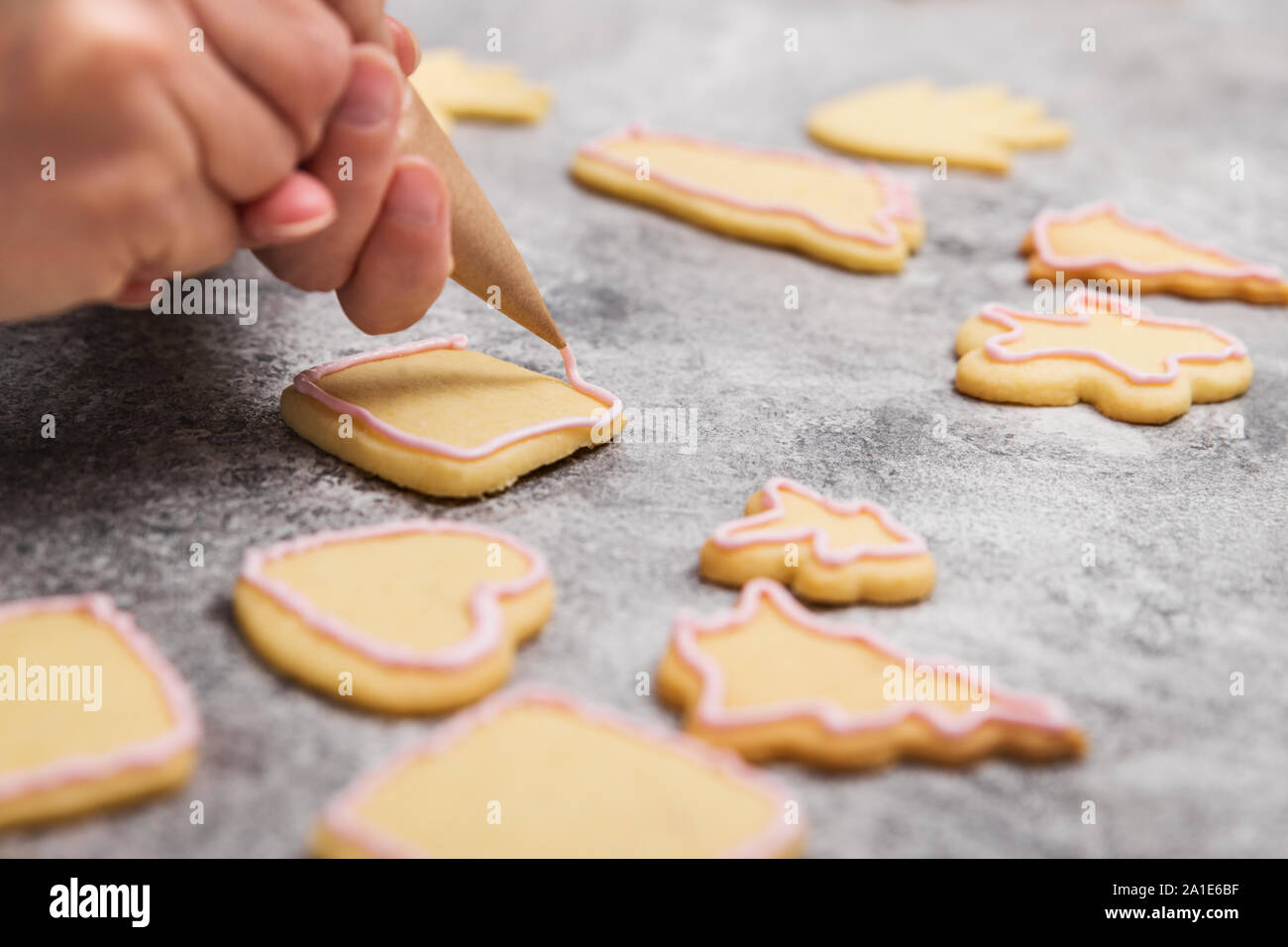 Female sugar baker is decoration christmas cookies with pink icing or frosting, workspace Stock Photo