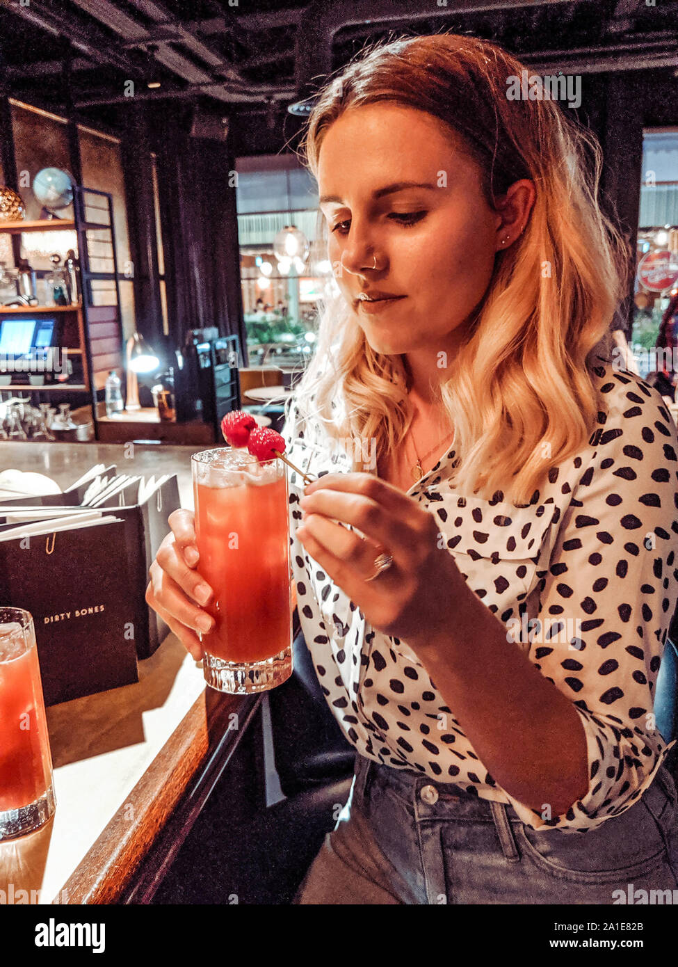 Woman in her twenties wearing dalmatian print shirt at a bar, drinking a cocktail Stock Photo