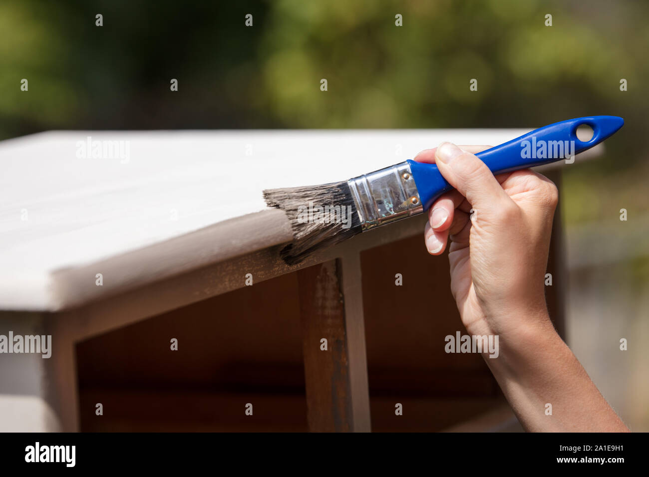 woman is painting an old cupboard outdoor, in white and grey shabby chic look Stock Photo