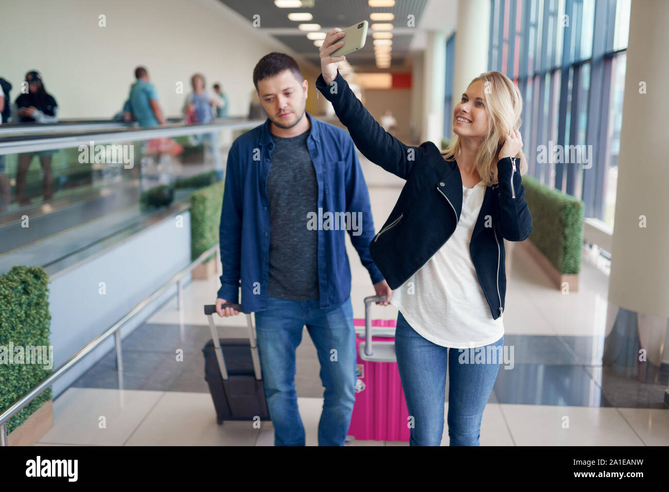 Photo of man carrying luggage and woman taking selfie walking in ...