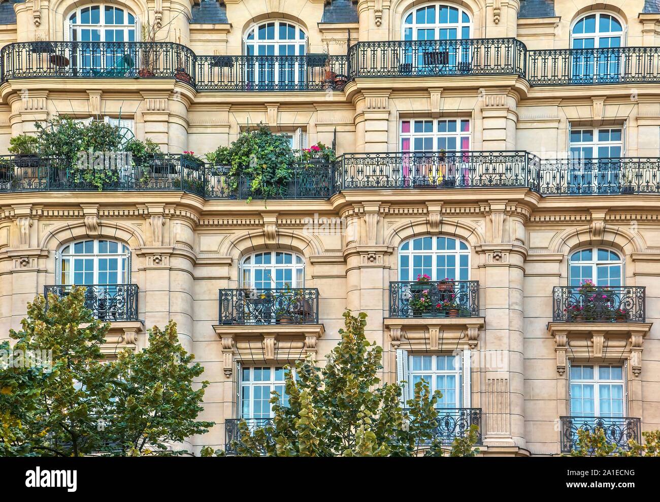 Street view of an old, elegant residential building facade in Paris, with ornate details in the stone walls, and french windows. Stock Photo