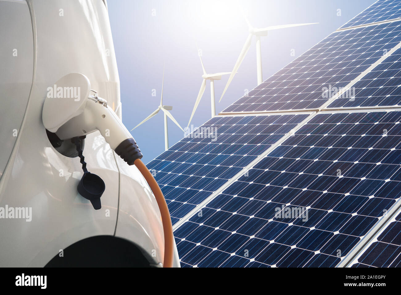 Close up of electric car with a connected charging cable on the background of solar panels and wind turbines - sources of clean renewable energy Stock Photo