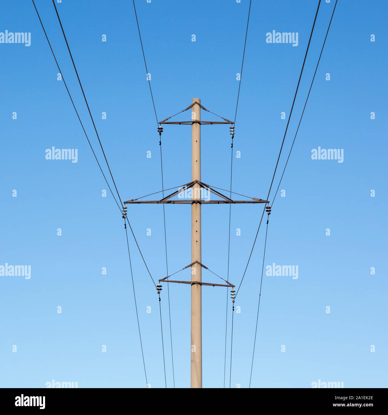 Concrete pillar power lines with steel traverses, porcelain insulators and high-voltage wires on a background of the clear blue sky Stock Photo