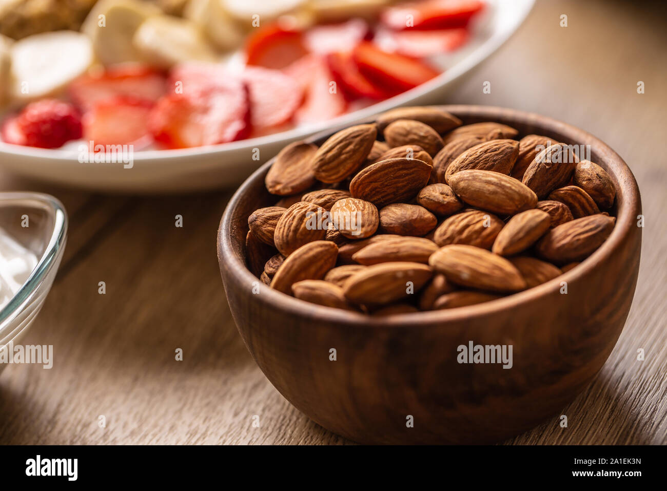 Almonds in wooden bowl with yoguth and plate of healthy breakfast Stock Photo