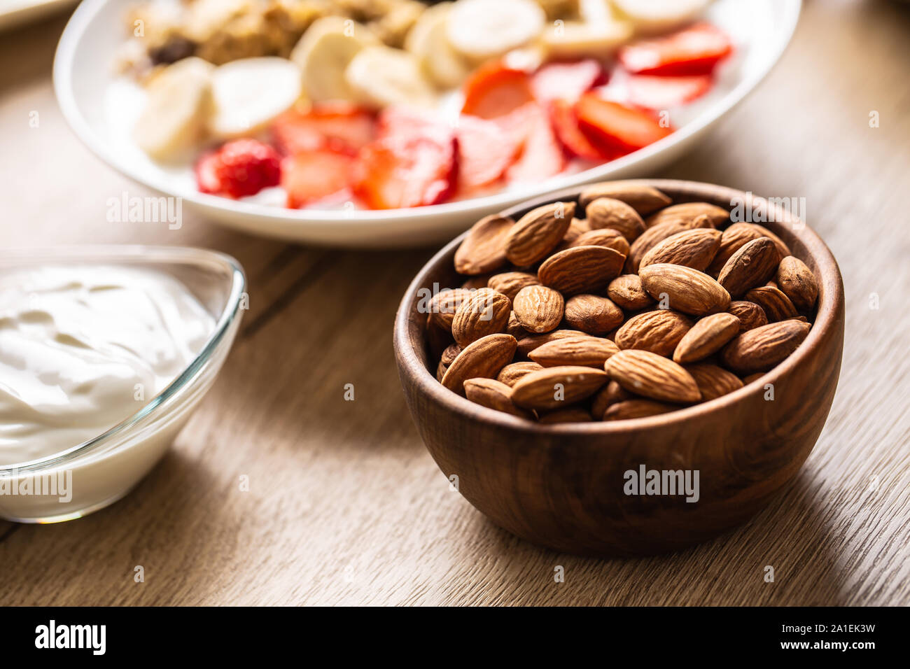 Almonds in wooden bowl with yoguth and plate of healthy breakfast Stock Photo