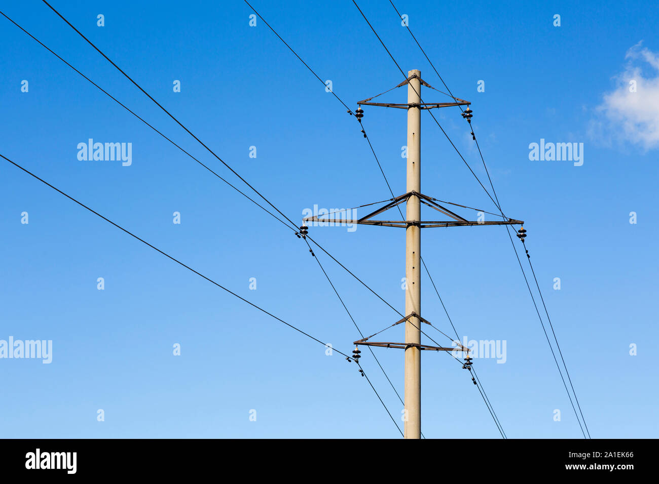 Concrete power line pylon with steel consoles, porcelain insulators and wires against a blue sky and white clouds Stock Photo