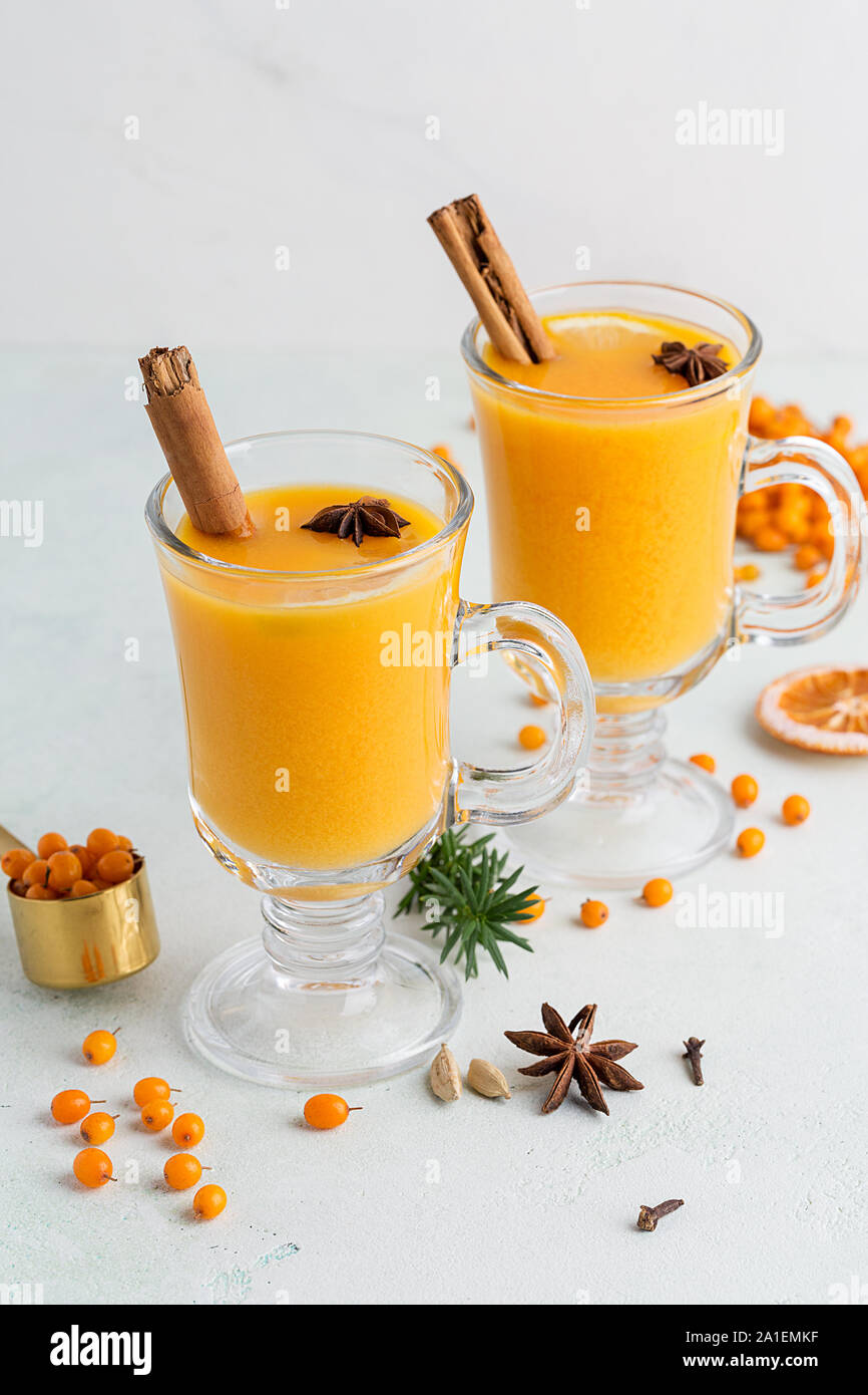 Two cups with sea buckthorn tea on white background with rosemary, cinnamon, buckthorn berries and orange near. Concept of medicinal beverage for heal Stock Photo