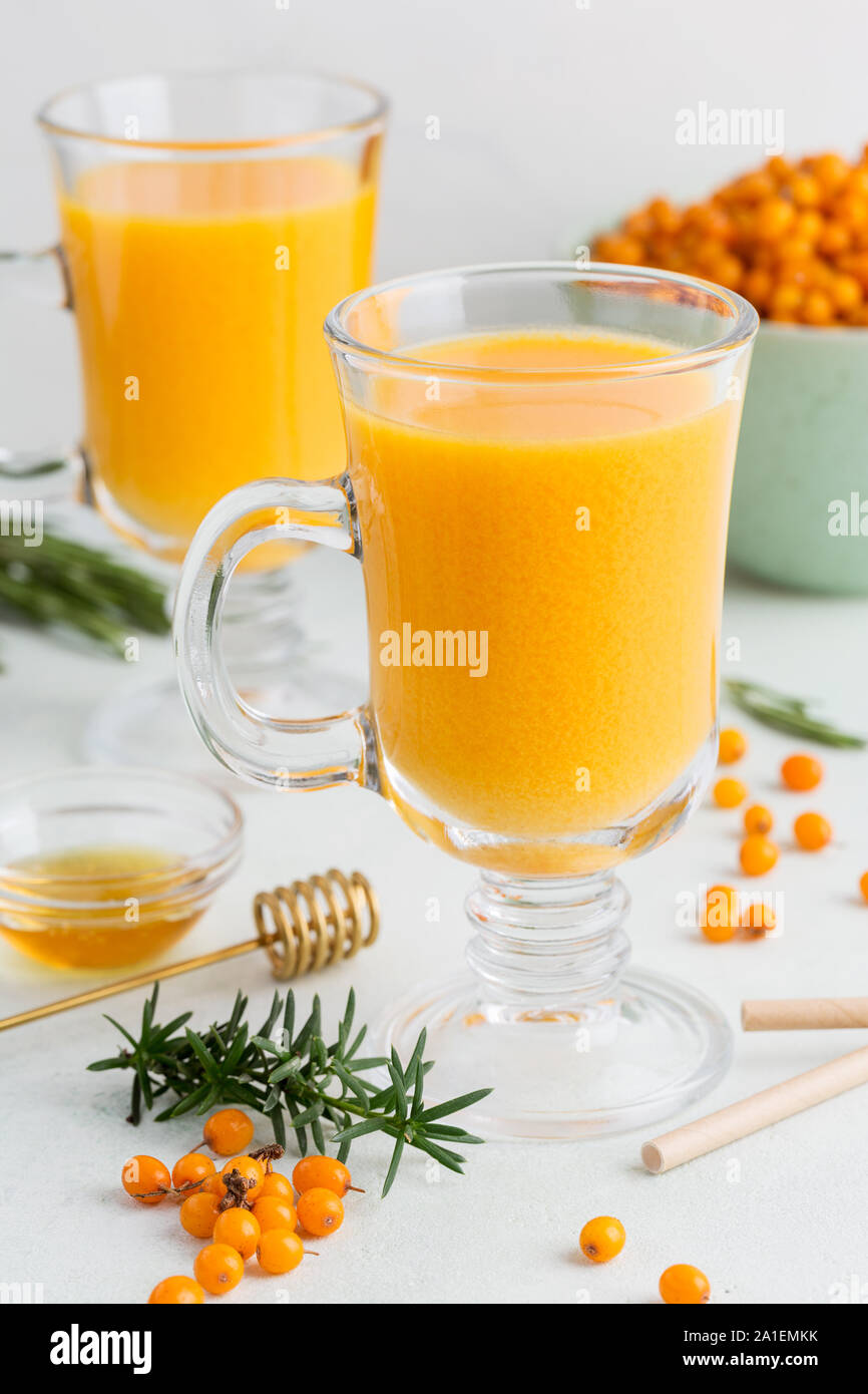 Sea buckthorn hot drinks in two glasses on white background. Concept of warm seasonal beverages. Honey and rosemary near. Side view Stock Photo