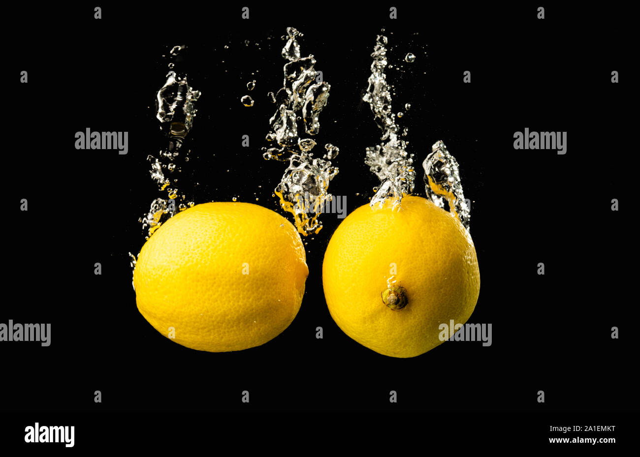 Fresh yellow lemons in water splash on black background with lots of air bubbles. Stock Photo