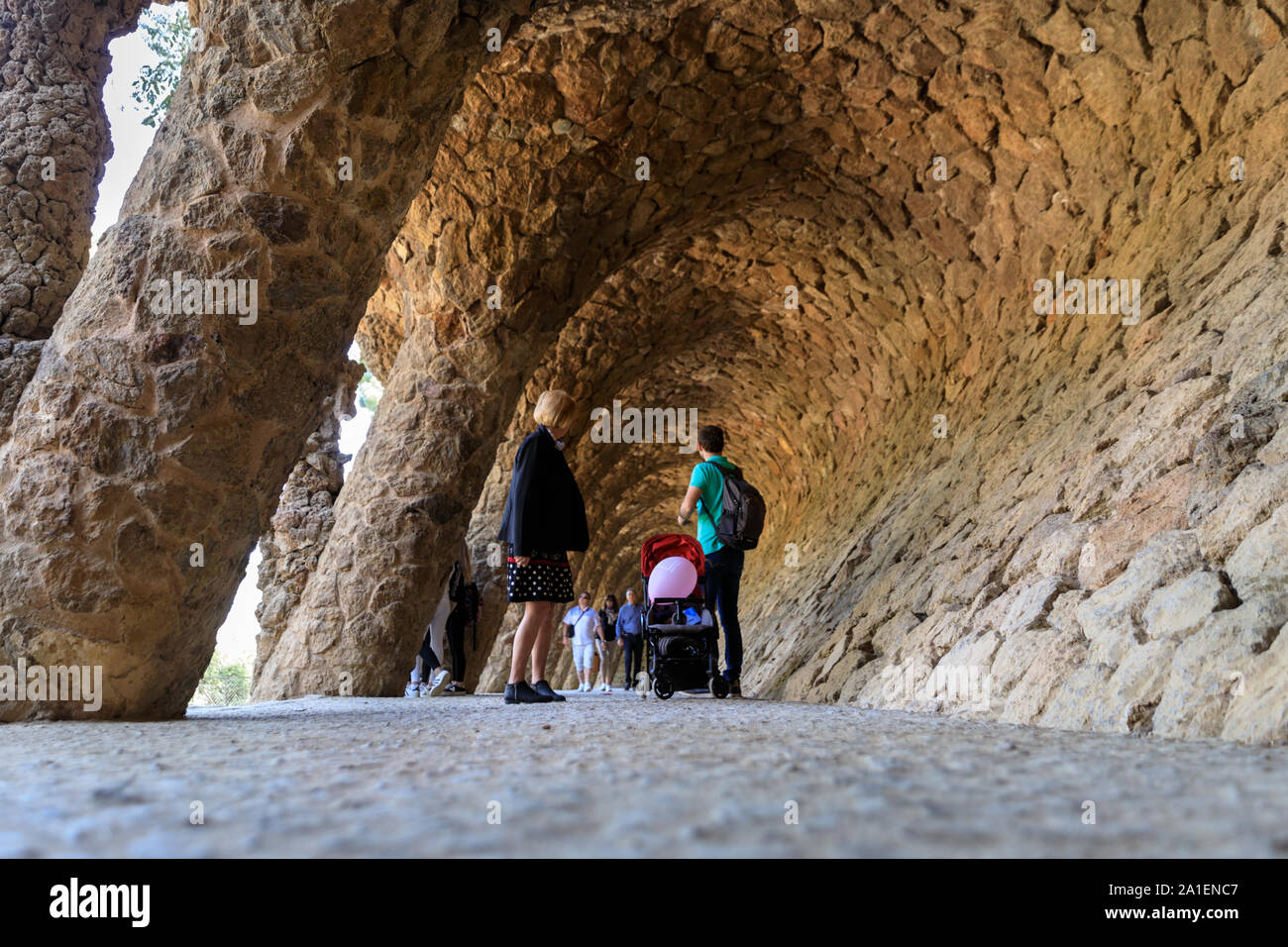 People walk through the colonnade of organic stone columns in Park Guell, designed by Antonio Gaudí Barcelona, Spain Stock Photo