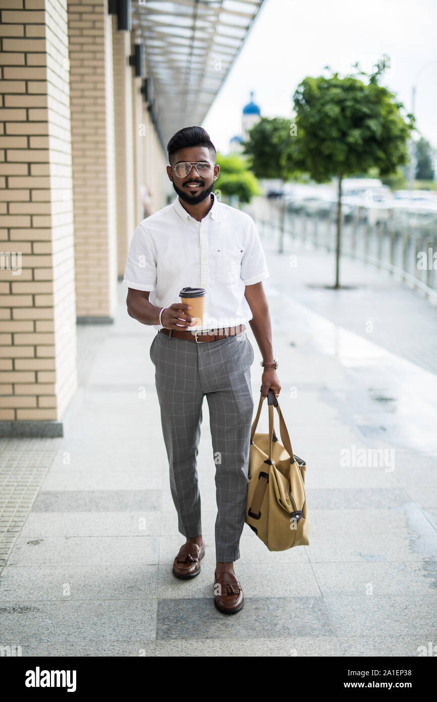 Young man with bag holding coffee while walking on the street Stock
