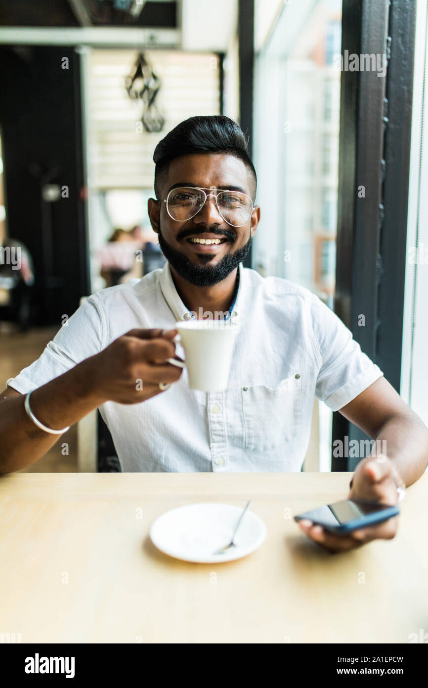 indian-man-use-phone-while-drink-coffee-in-cafe-2A1EPCW.jpg