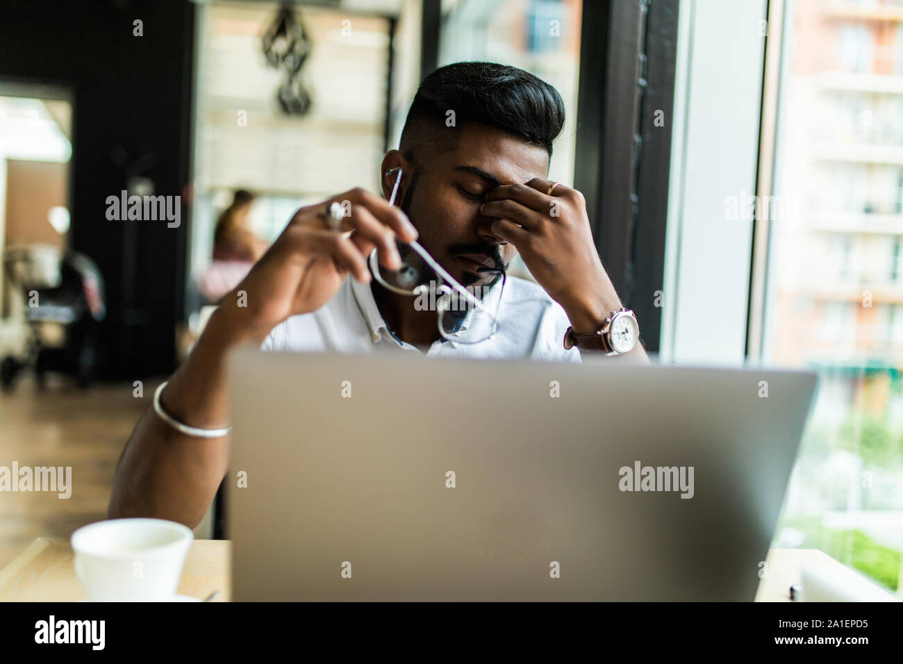Young Asian businessman suffering from tired eyes after long hours of using laptop. Stock Photo