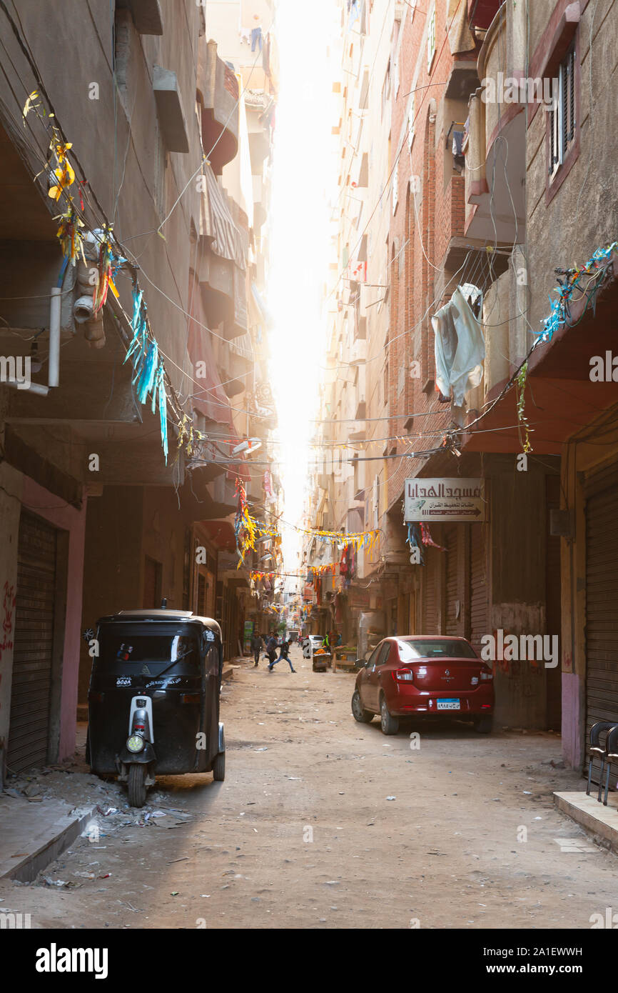Alexandria, Egypt - December 18, 2018: Alexandria street view, ordinary people walk the street with parked auto rickshaw and cars, vertical photo Stock Photo